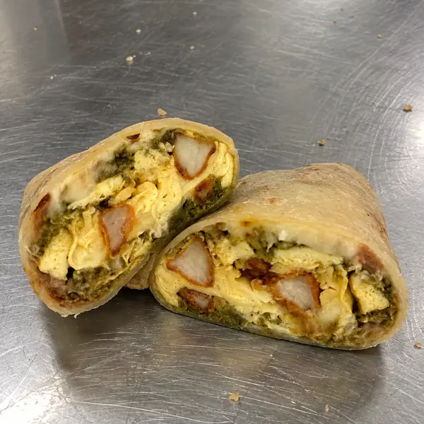 Phone photo of a breakfast burrito cut in half on a scratched steel kitchen counter with crumbs